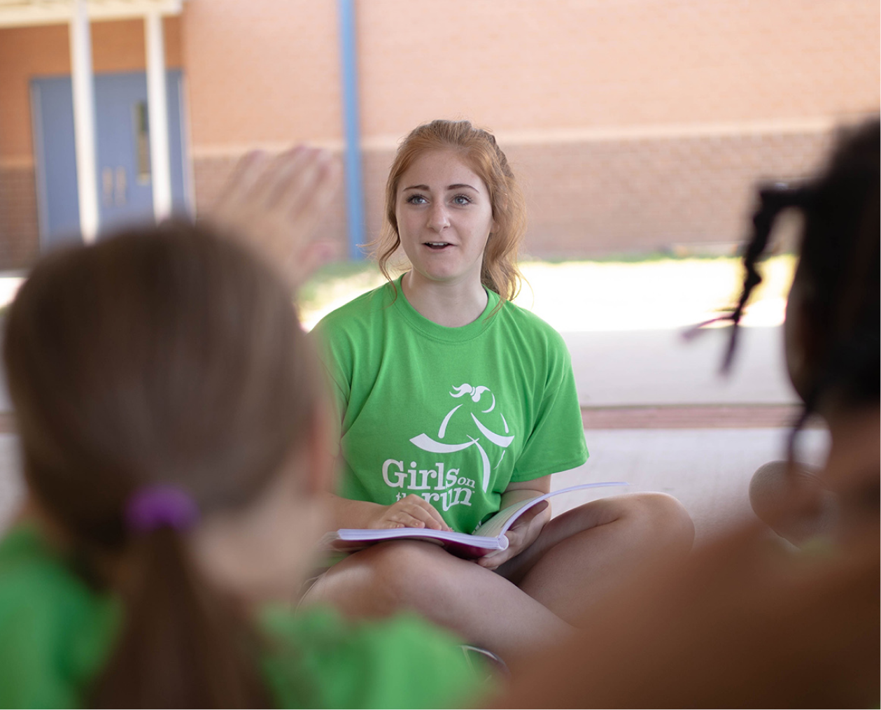 Girls on the Run junior coach is happily asking question to the program participants outdoors